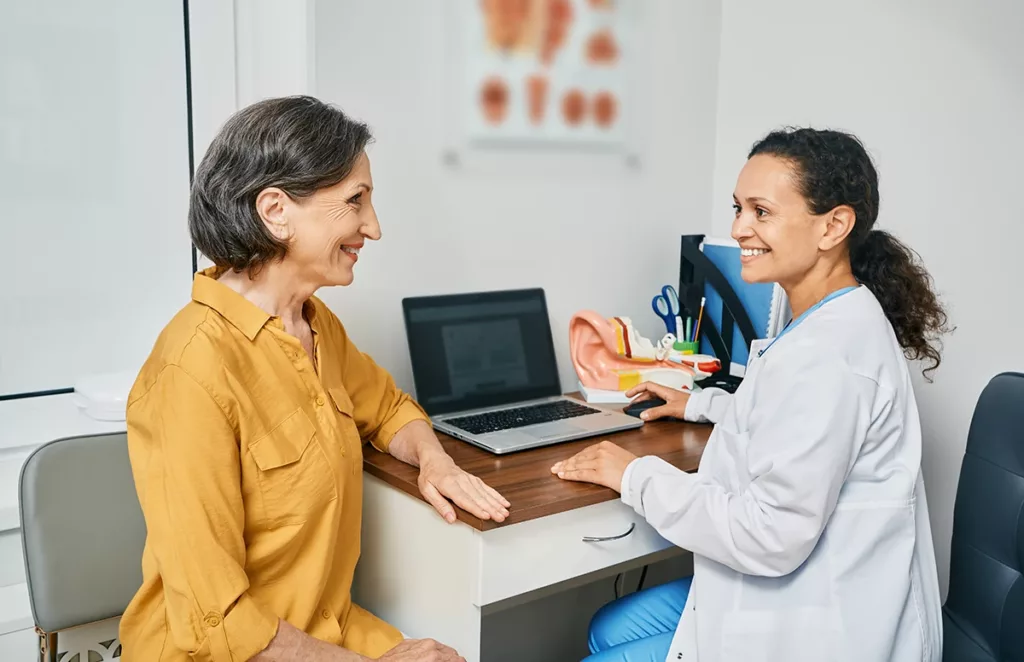 An older adult women in a hearing clinic happily undergoing her yearly hearing exam as recommended by her hearing care specialist.